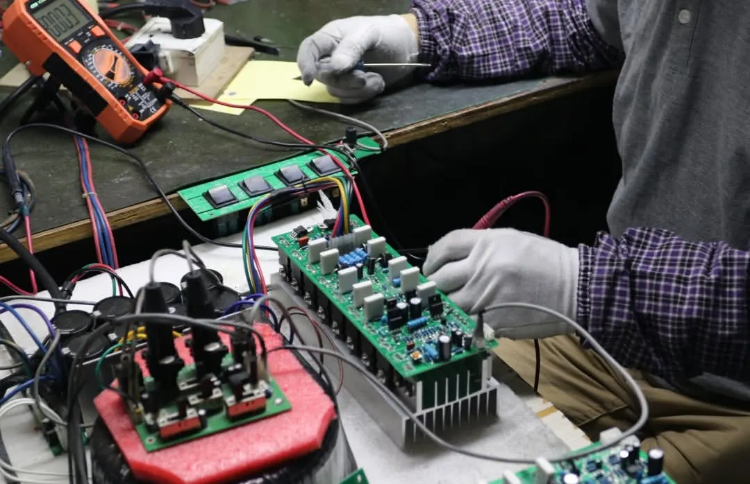 Precision PCB Calibration & Multimeter Voltage Verification ELM Audio technician measuring power amplifier PCB circuitry with digital multimeter and heatsink assembly in factory workshop