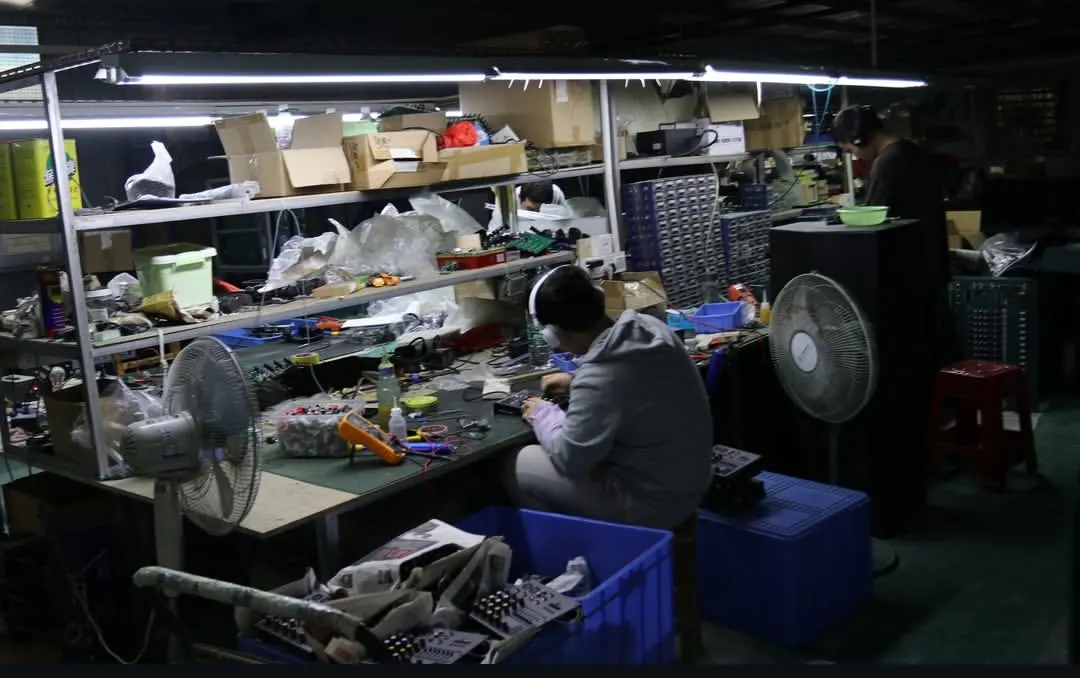 Mixer Console Assembly & Multi-Station Production Floor ELM Audio production floor showing technicians assembling audio consoles and loudspeaker cabinets with cooling ventilation